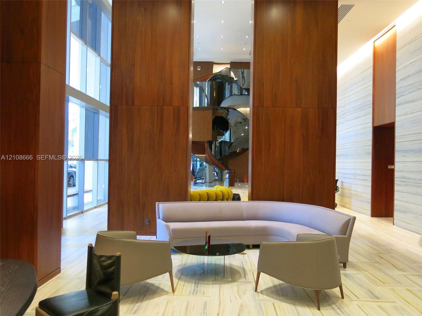 Grand foyer featuring double-height ceilings, floor-to-ceiling wood paneling, large-format stone flooring, integrated recessed lighting, and a sculptural spiral staircase
