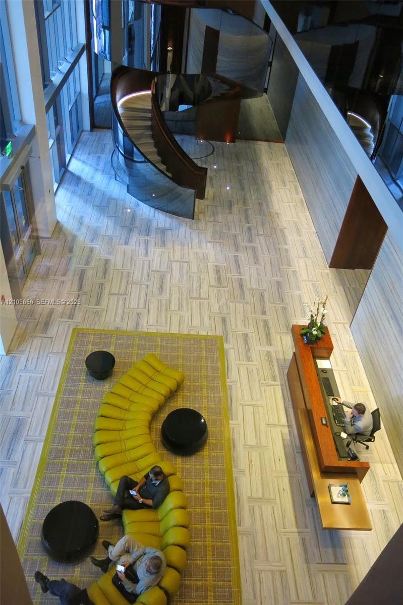Double-height ceiling, sculptural spiral staircase with glass railing, stone tile flooring, and integrated wood-finish reception desk