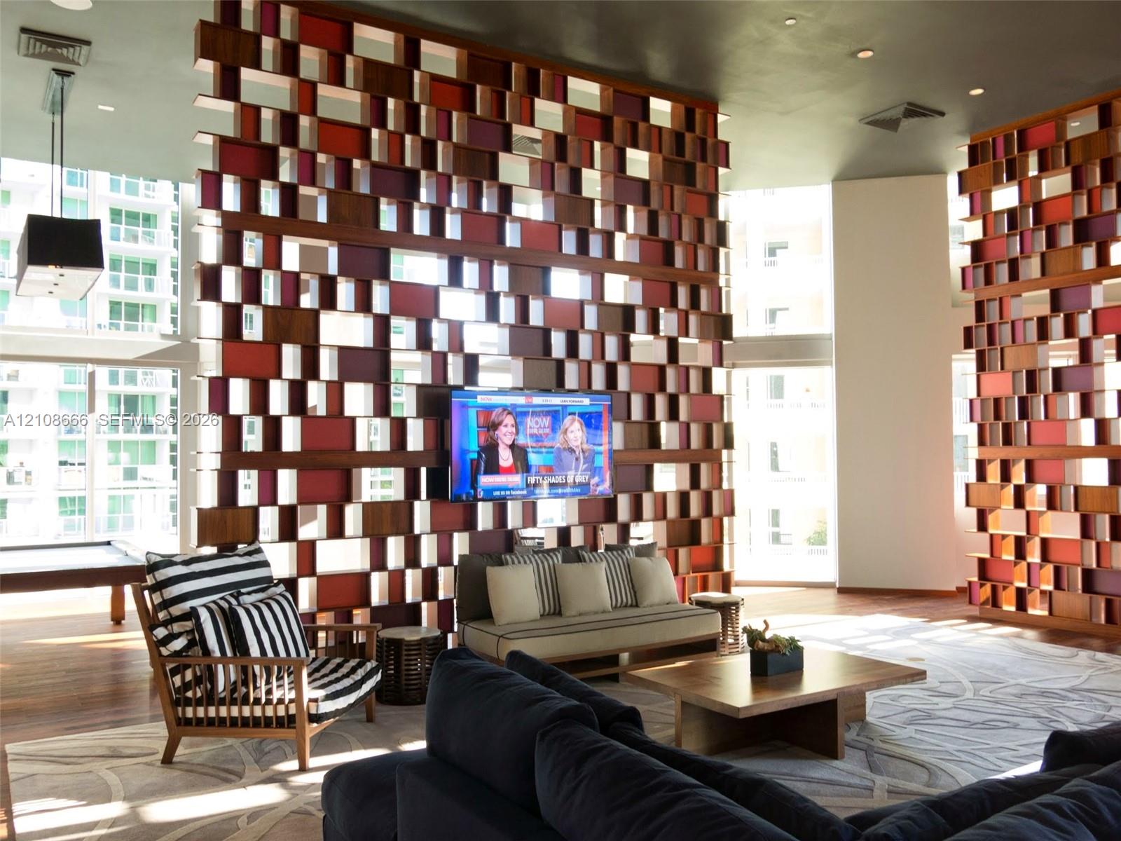 Custom wood-grid architectural room divider with integrated television mount and high ceilings featuring recessed lighting
