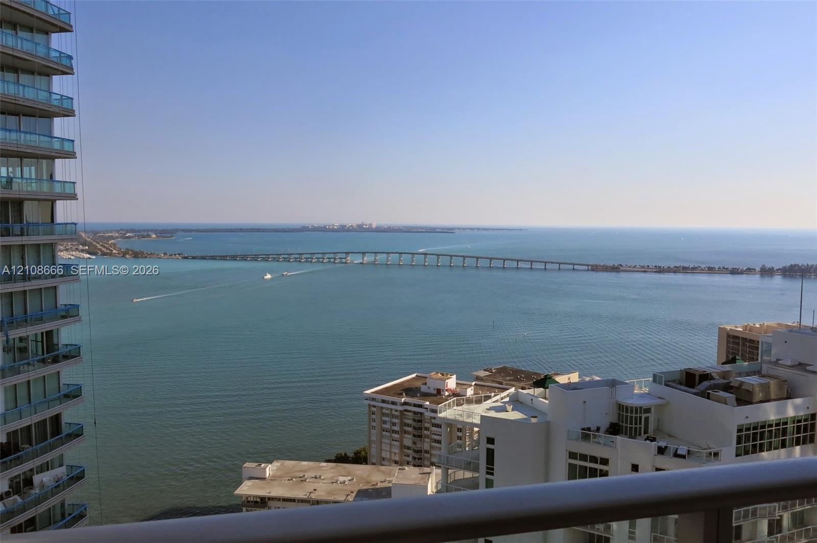 Elevated balcony with a horizontal metal railing overlooking a maritime horizon, bridge, and coastal cityscape