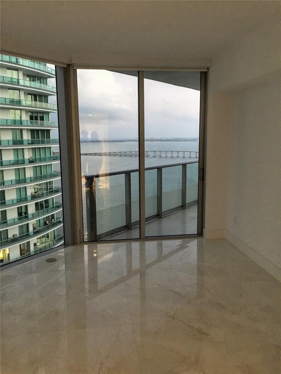 Floor-to-ceiling glass sliding doors, stone-finish flooring, and a private balcony featuring a glass railing and water backdrop Floor-to-ceiling glass sliding doors, stone-finish flooring, and a private balcony featuring a glass railing and water backdrop