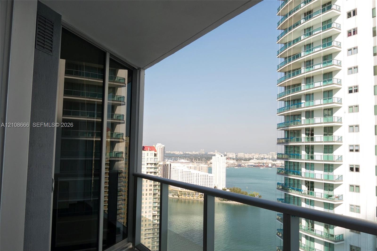 Private balcony with a metal and glass railing, floor-to-ceiling glass sliding door, and urban and water scenery Private balcony with a metal and glass railing, floor-to-ceiling glass sliding door, and urban and water scenery