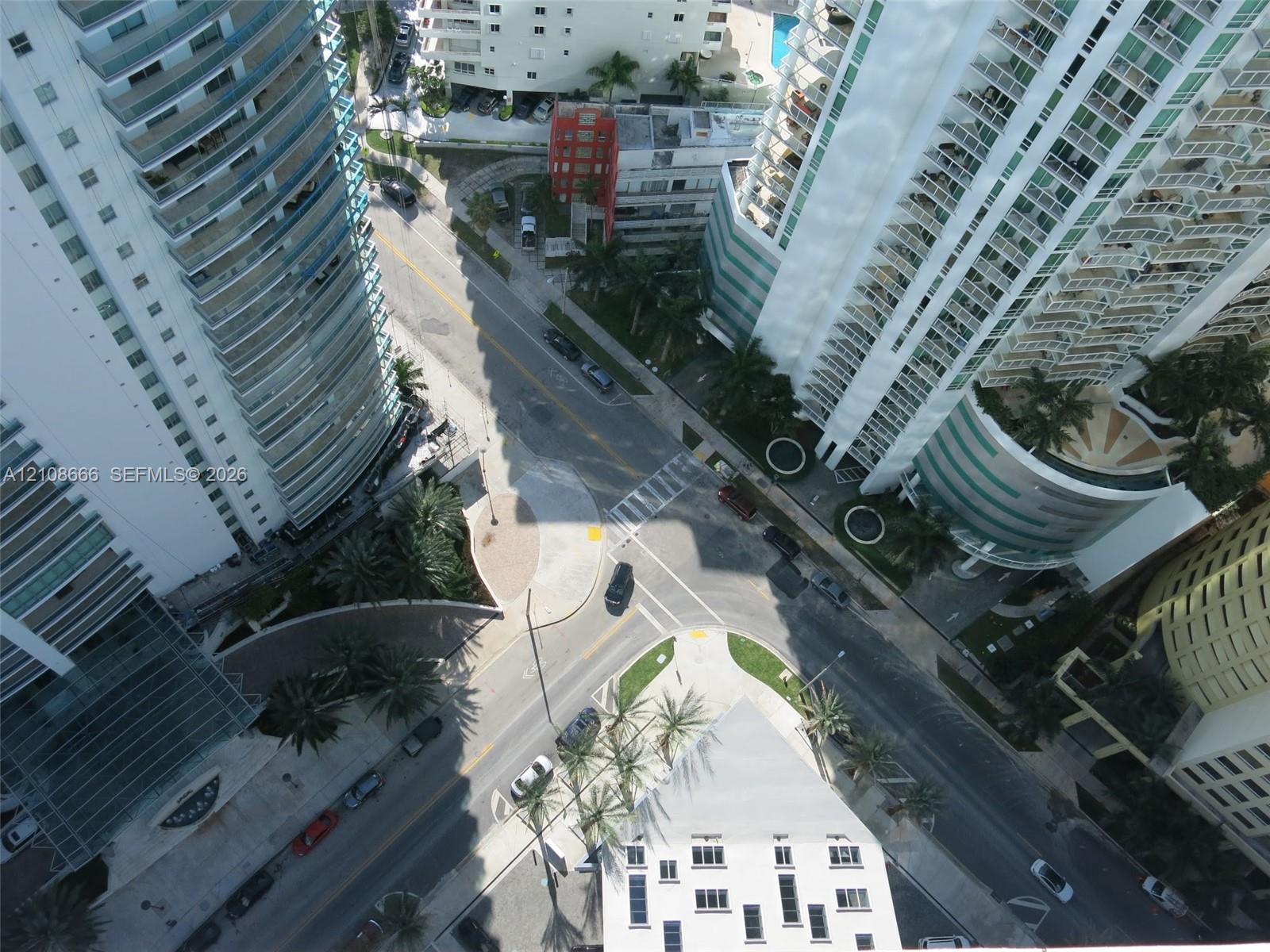High-rise urban setting featuring tiered glass balconies, multi-story structural architecture, palm tree landscaping, and paved street-level infrastructure