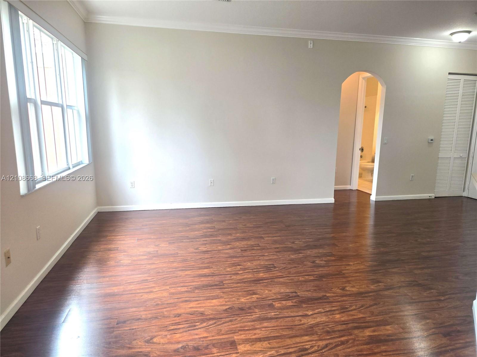 Wood-finish flooring, neutral wall tones, crown molding, multi-pane windows, and a classic arched doorway