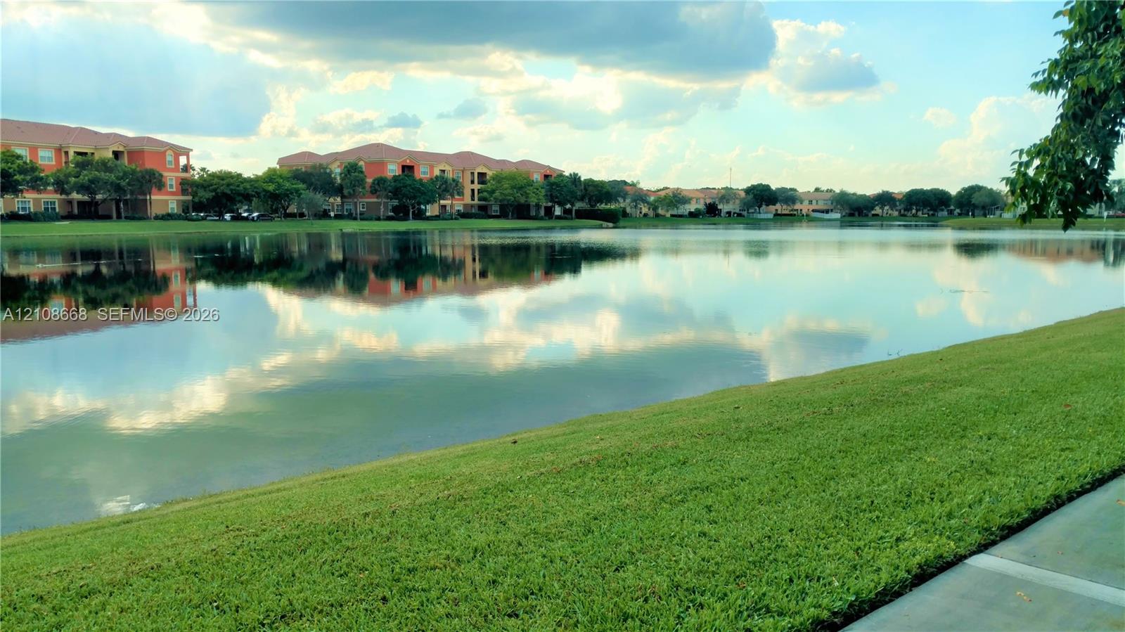 Expansive lakefront setting featuring a manicured lawn and concrete walking path