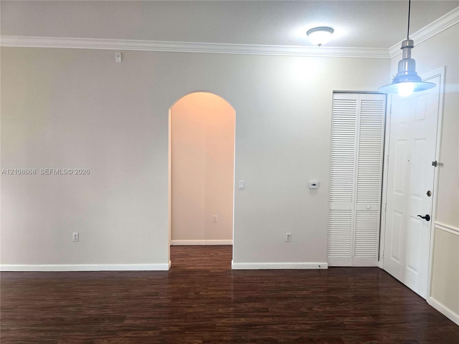 Interior space featuring wood-finish flooring, an arched architectural opening, crown molding, a louvered bi-fold closet door, and a metal pendant light fixture