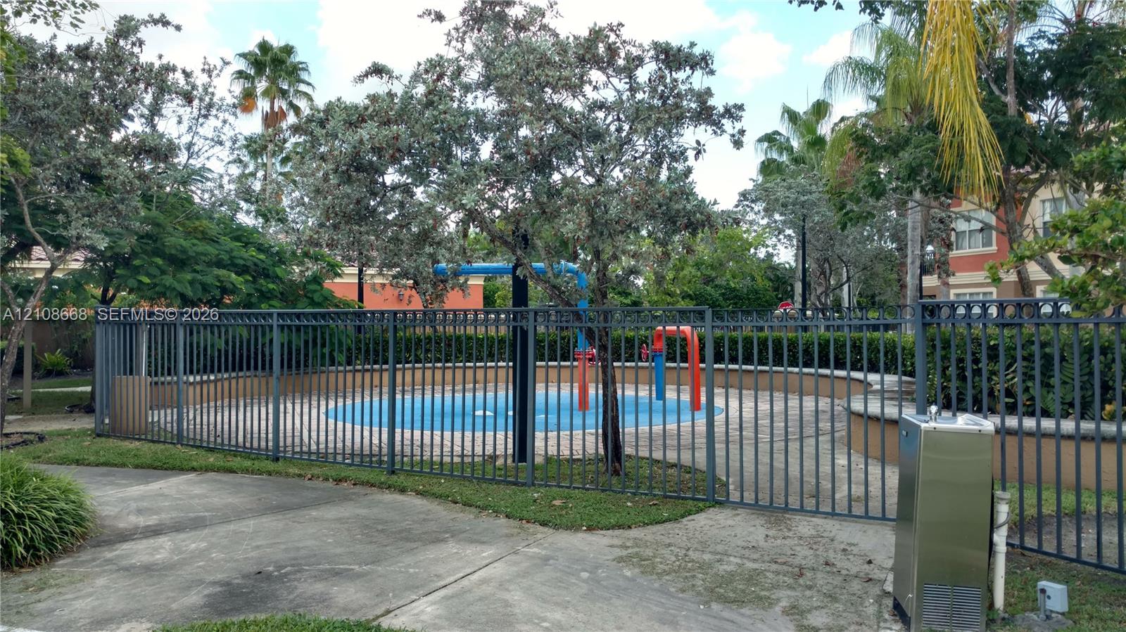 Outdoor splash pad featuring a concrete deck, built-in water features, and a metal perimeter fence