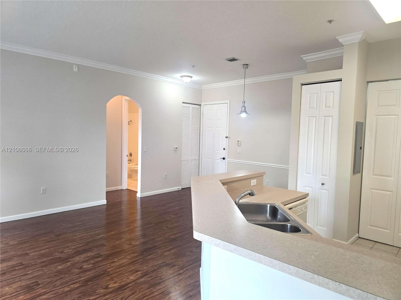Open-concept interior featuring wood-finish flooring, a kitchen breakfast bar with integrated double-basin stainless steel sink, crown molding, and an arched entry