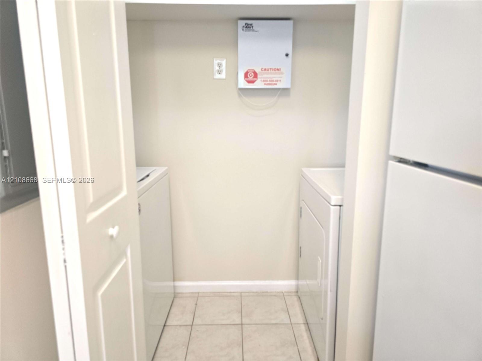 Utility closet featuring tiled flooring, bi-fold doors, and a wall-mounted security panel