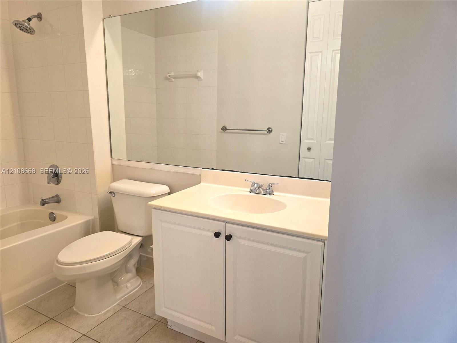 Bathroom featuring a white vanity cabinet, solid-surface countertop with an integrated sink, full-width wall mirror, and a tile-surround combination tub and shower