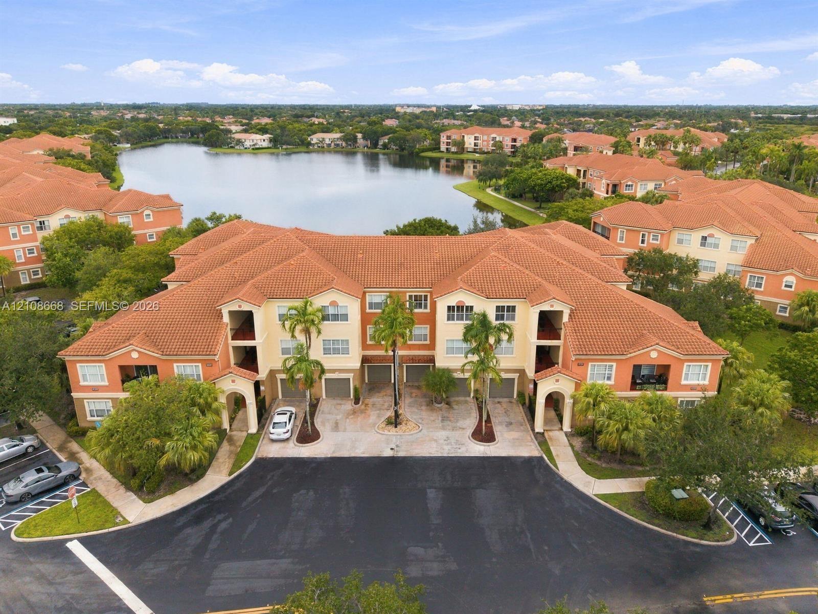 Multi-story building featuring a terracotta-tiled roof, stucco exterior, integrated garage access, and mature palm tree landscaping