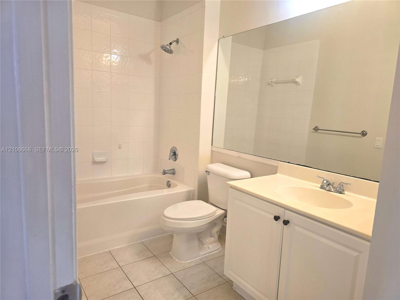 Full bathroom featuring a tub-shower combination with tile surround, vanity with an integrated basin, large wall-mounted mirror, and tile flooring