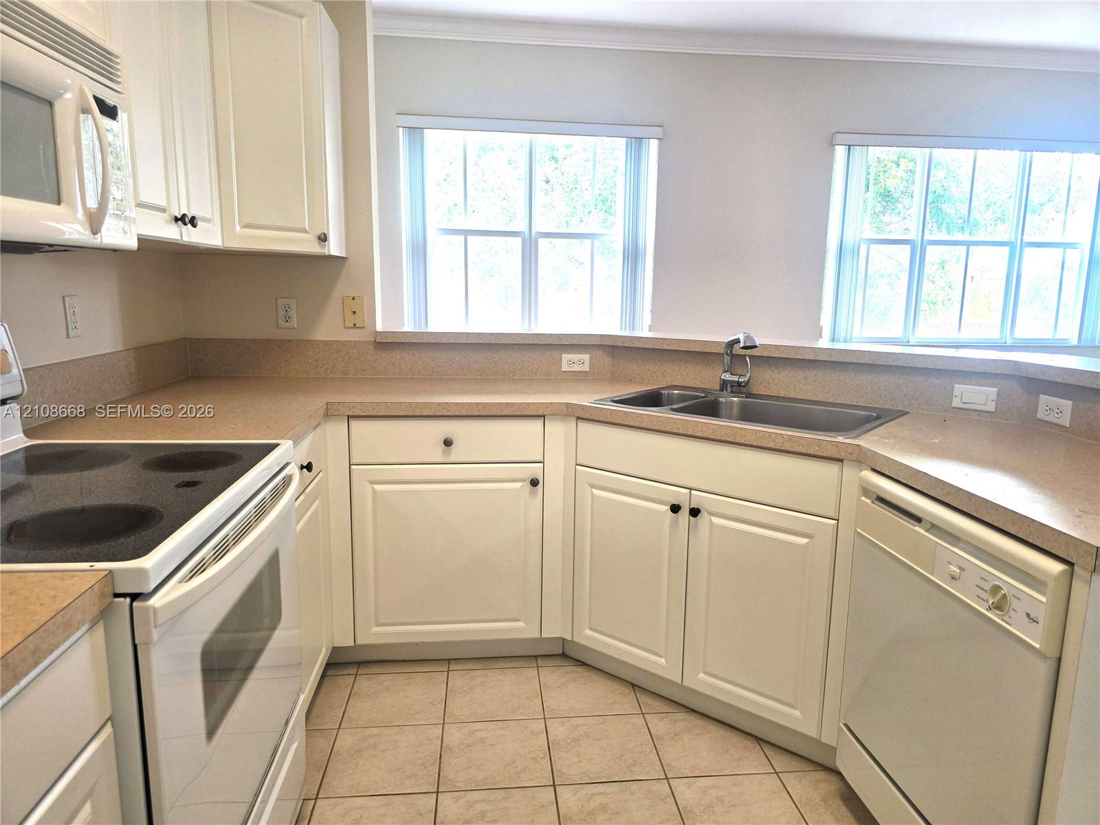 Kitchen featuring white shaker-style cabinetry, solid-surface countertops, a stainless steel double-basin sink, and ceramic tile flooring
