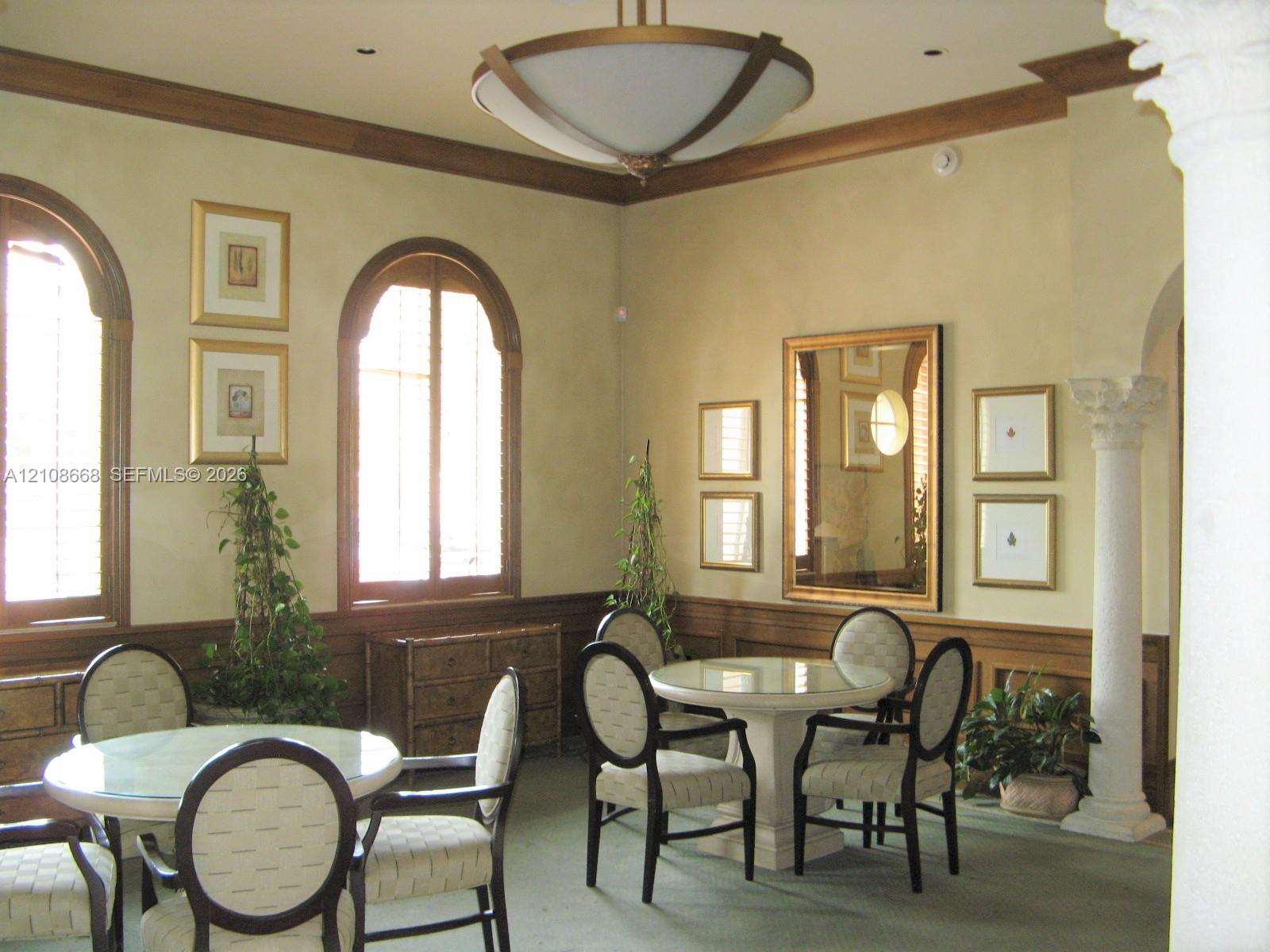 Interior space featuring arched windows with wood-trim detailing, decorative crown molding, a central modern chandelier, and a structural column with a Corinthian-style capital