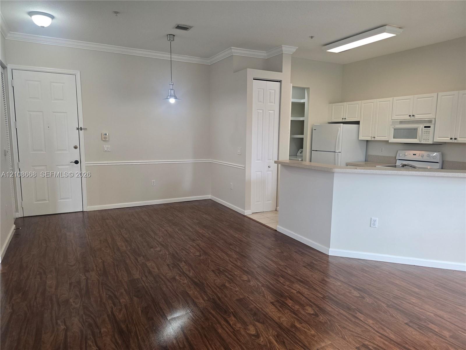 Open-concept area featuring wood-finish flooring, crown molding, chair rail detailing, white cabinetry, and a peninsula-style kitchen counter