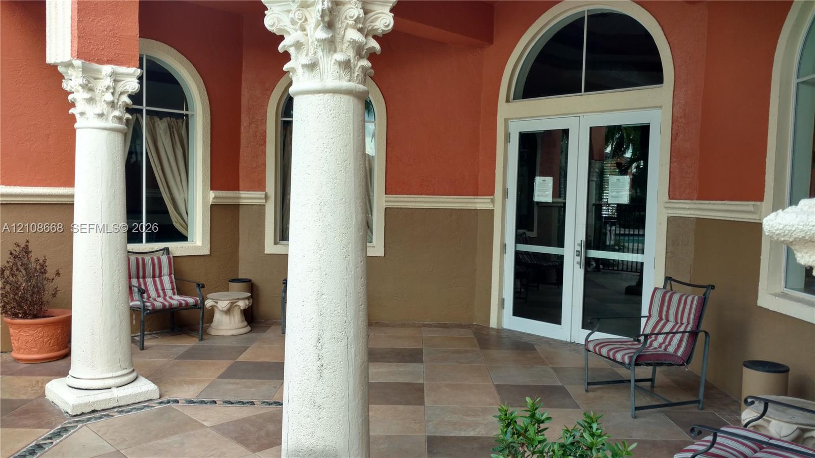 Covered patio featuring decorative Corinthian-style columns, arched window detailing, and multi-toned tile flooring