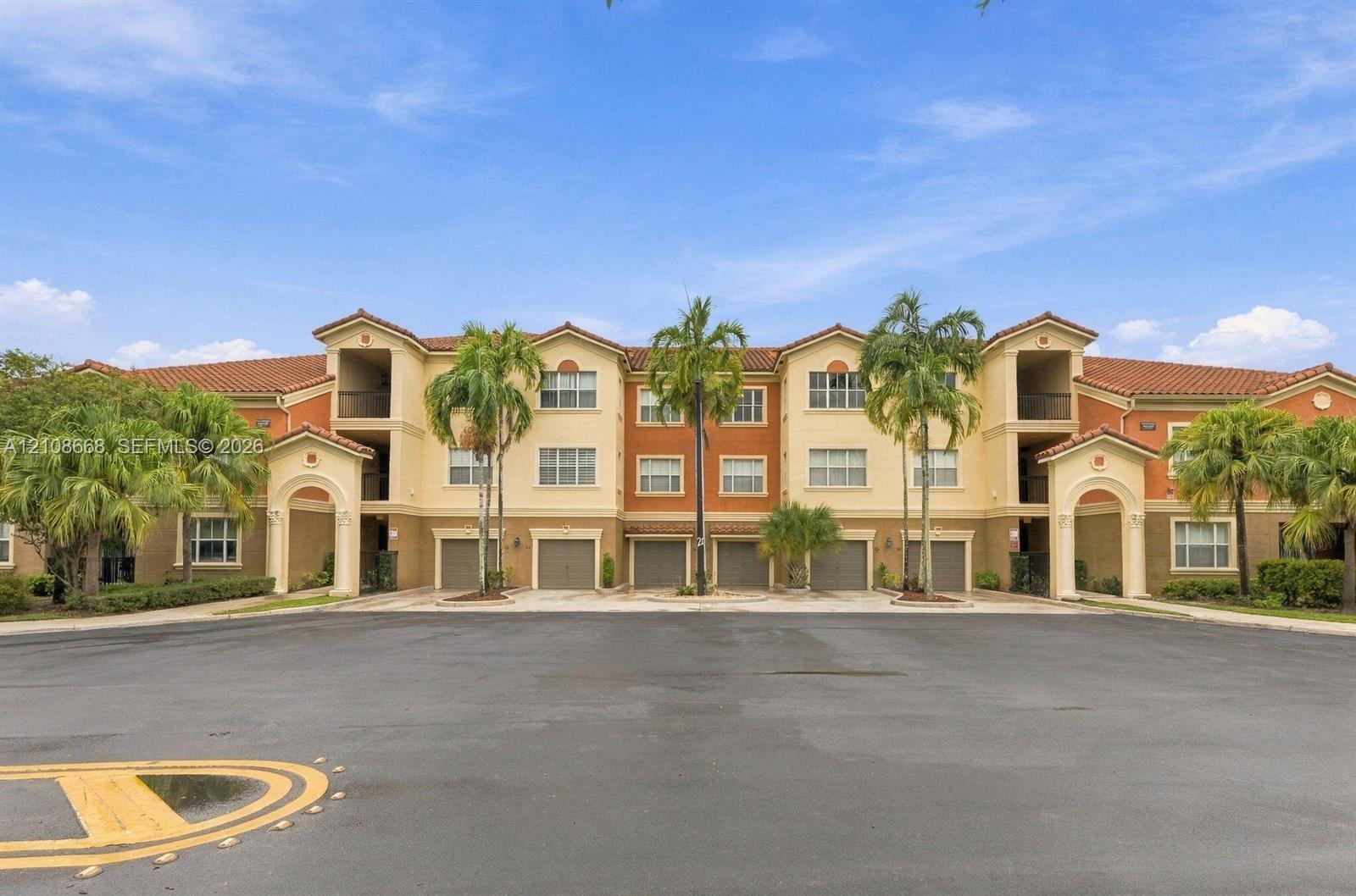 Multi-story exterior featuring a Mediterranean-style tile roof, stucco facade, arched entryway detailing, and multiple integrated garage bays