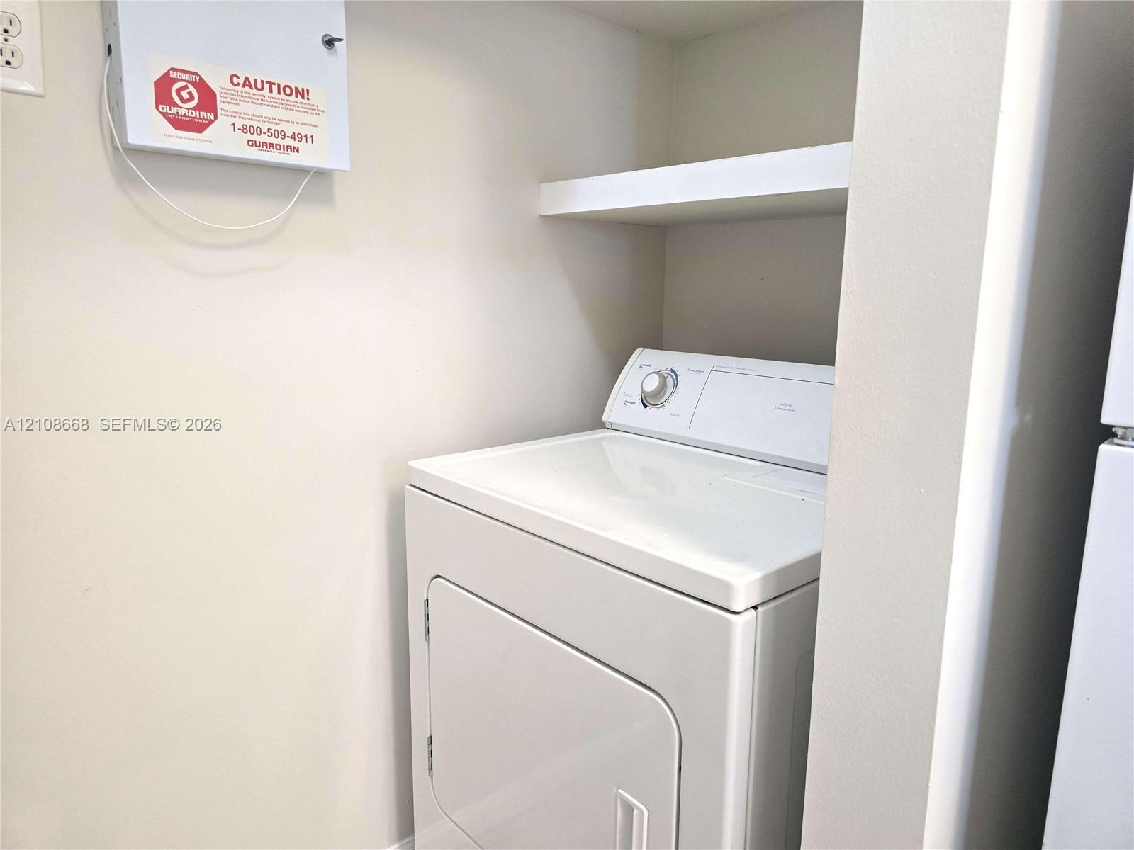 Built-in laundry alcove featuring overhead shelving and an integrated security system wall panel
