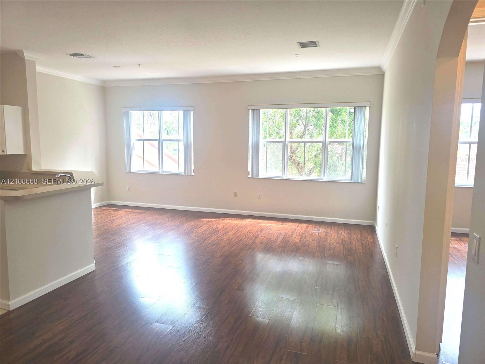 Open interior featuring wood-finish flooring, crown molding, double-pane windows, and a pass-through counter