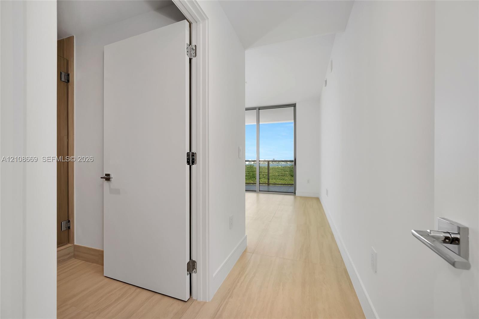 Interior space featuring wood-finish flooring, white walls, flush-panel doors, modern lever-style hardware, and floor-to-ceiling sliding glass doors