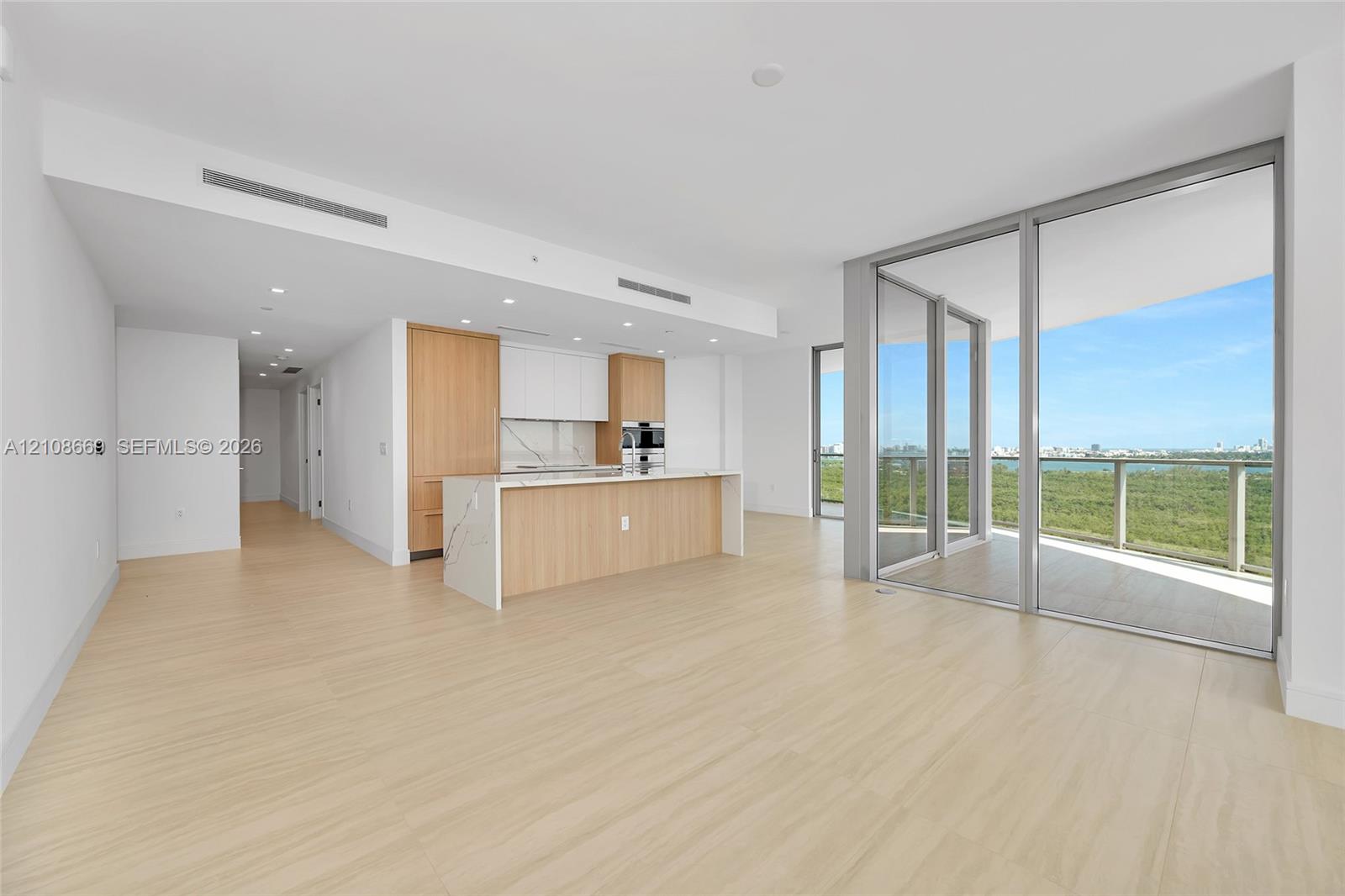 Open-concept interior featuring wood-finish flooring, kitchen island with stone-surface countertop, floor-to-ceiling glass sliding doors, and built-in stainless steel wall oven
