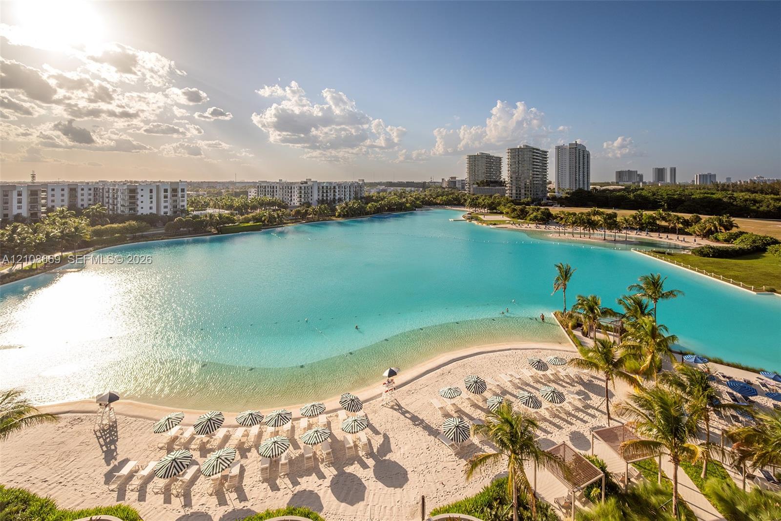 Expansive man-made lagoon featuring sandy beach shorelines, palm tree landscaping, and surrounding multi-story residential structures