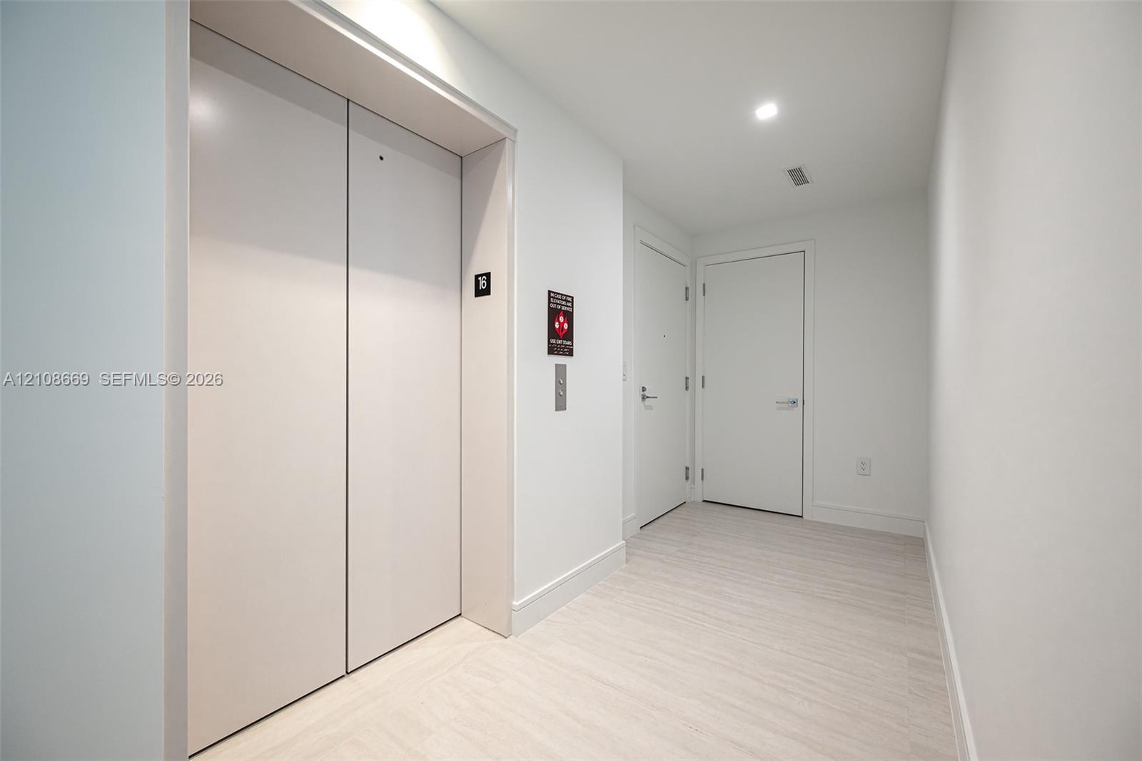 Elevator foyer featuring smooth-finish ceiling with recessed lighting, light-toned wood-finish flooring, and minimalist white interior doors
