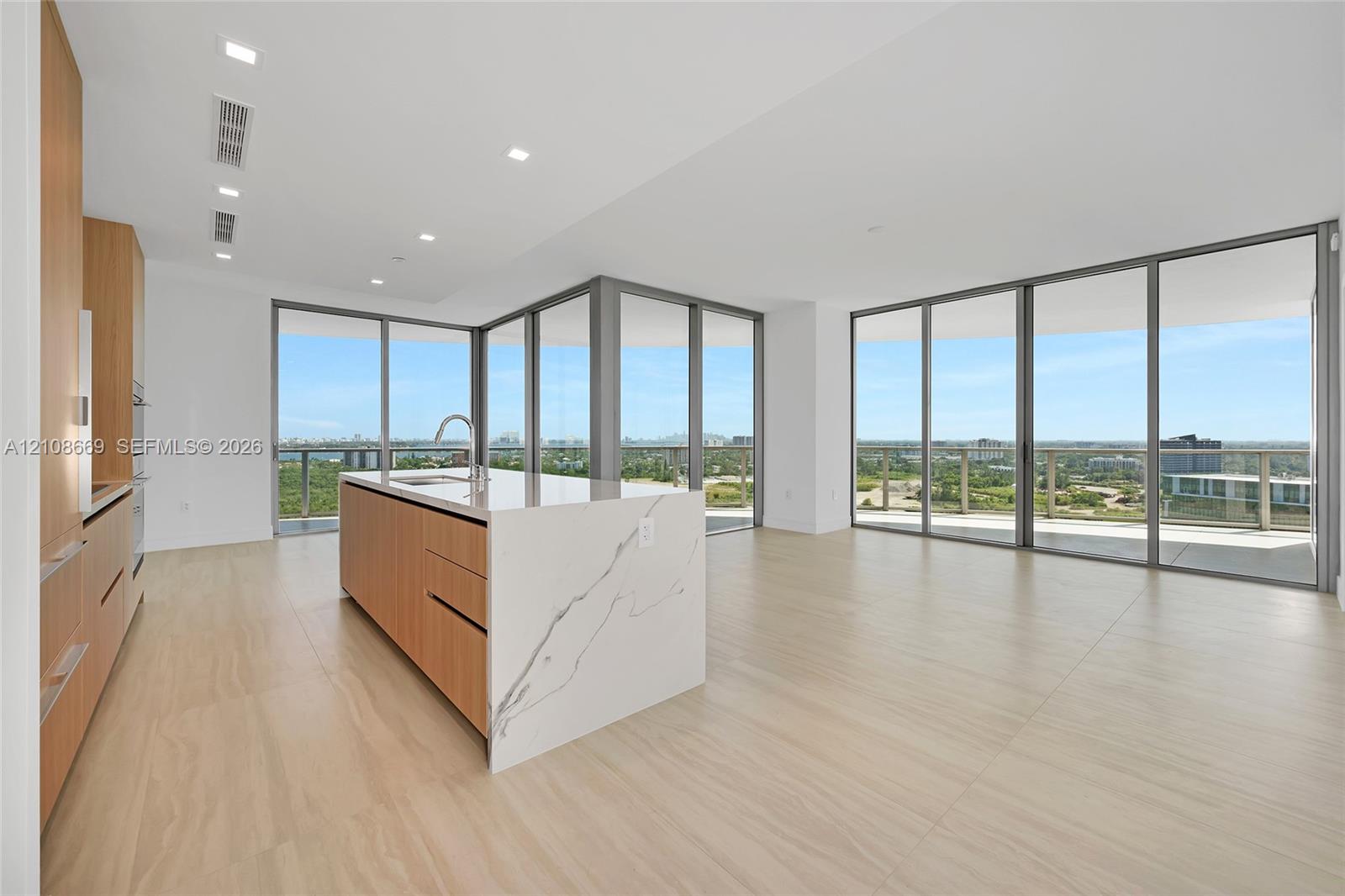 Kitchen featuring a waterfall island with a stone-finish countertop, flat-panel wood-finish cabinetry, floor-to-ceiling glass wall panels, and light-toned tile flooring