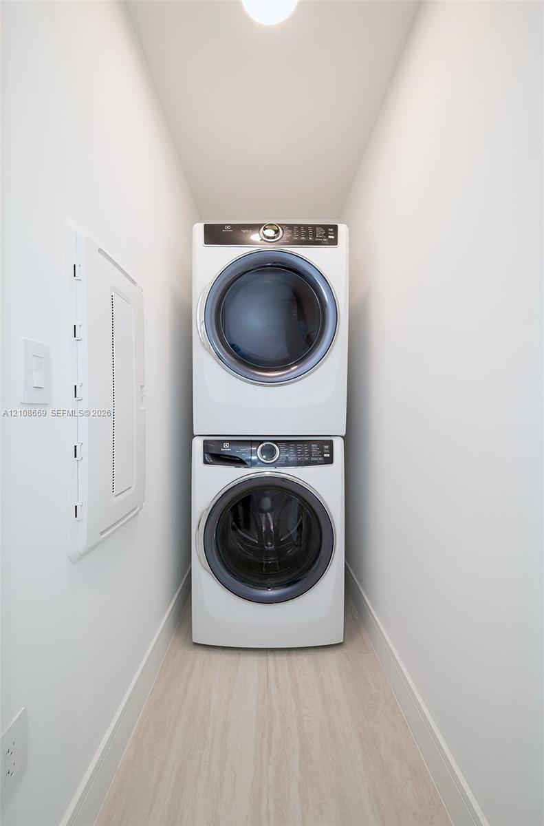 Dedicated laundry alcove featuring a stacked white front-loading washer and dryer set on light-toned wood-finish flooring