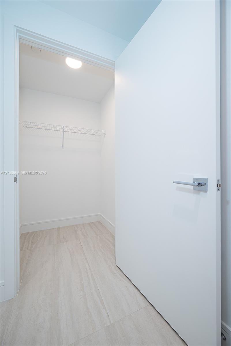 Walk-in storage space featuring wood-finish flooring, a white flat-panel door with a square-back plate lever handle, and a mounted wire shelving system
