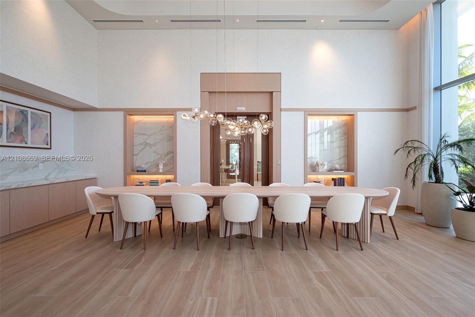 Double-height ceilings featuring recessed lighting, floor-to-ceiling windows, light wood-finish flooring, custom built-in cabinetry with stone slab accents, and a sculptural multi-globe pendant light fixture