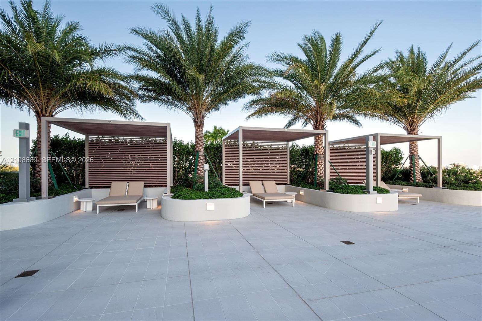 Outdoor terrace featuring large-format tile flooring, three overhead architectural pergolas with integrated horizontal wood-slat privacy screens, and raised concrete planters containing mature palm trees and lush greenery