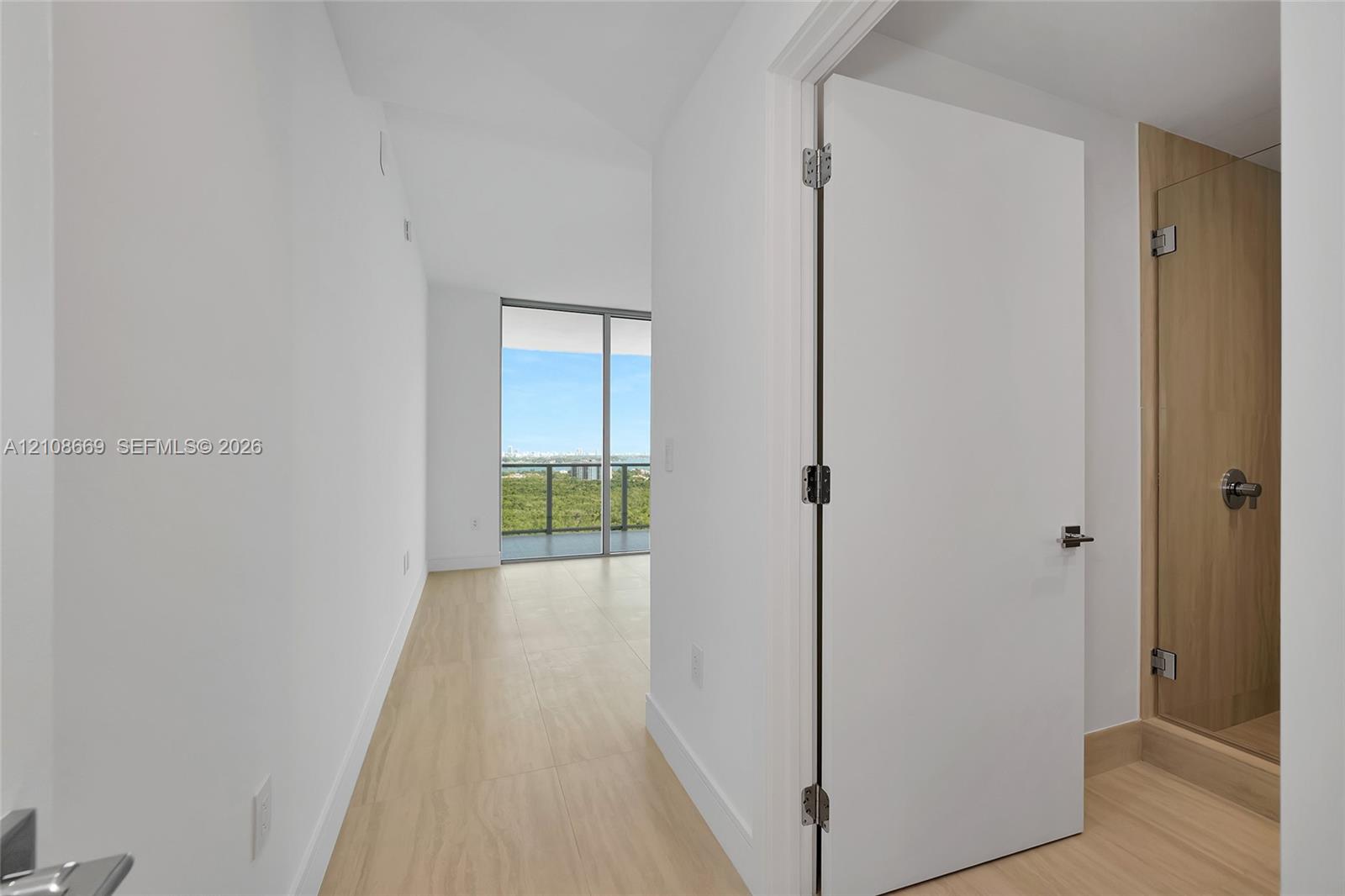 Interior featuring light wood-finish flooring, floor-to-ceiling glass sliding doors, and a glass-enclosed shower with wood-tone surround
