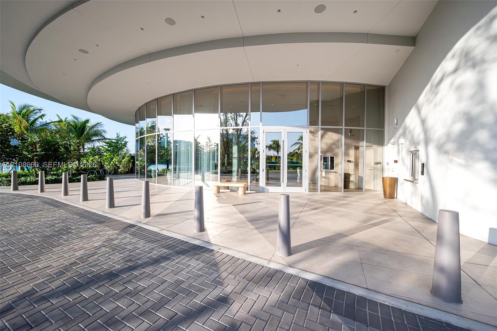 Curved floor-to-ceiling glass facade featuring an expansive covered porte-cochre, large-format tile flooring, and integrated recessed ceiling lighting