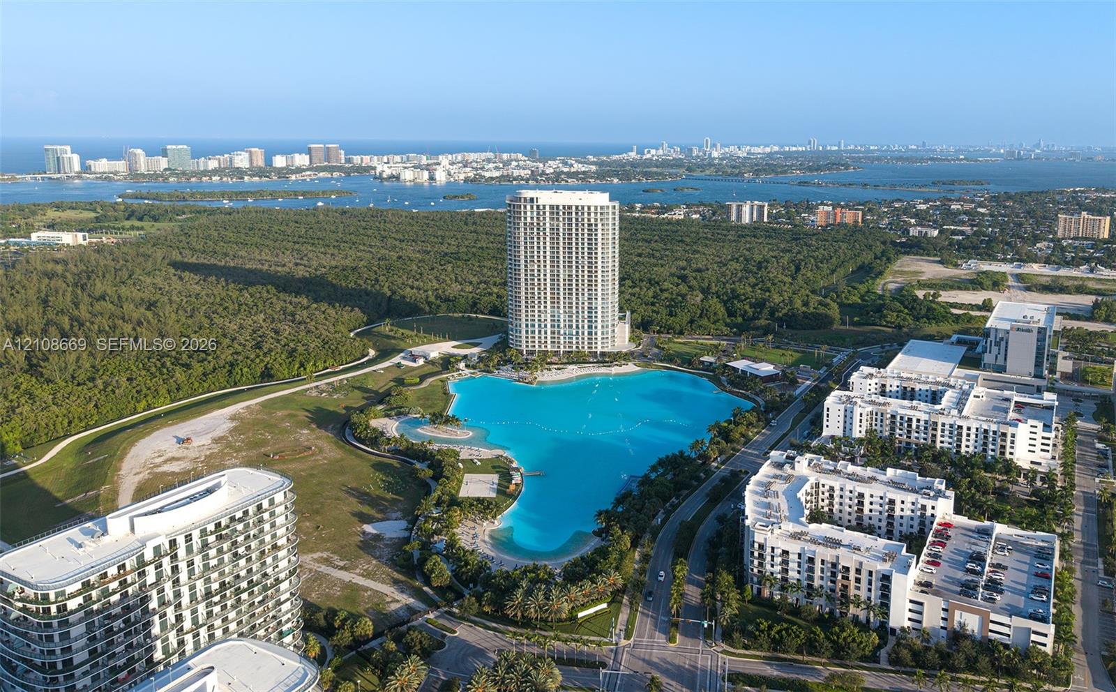 Aerial perspective of a high-rise residential complex featuring a large turquoise lagoon, landscaped grounds, multi-story buildings, and proximity to coastal water bodies