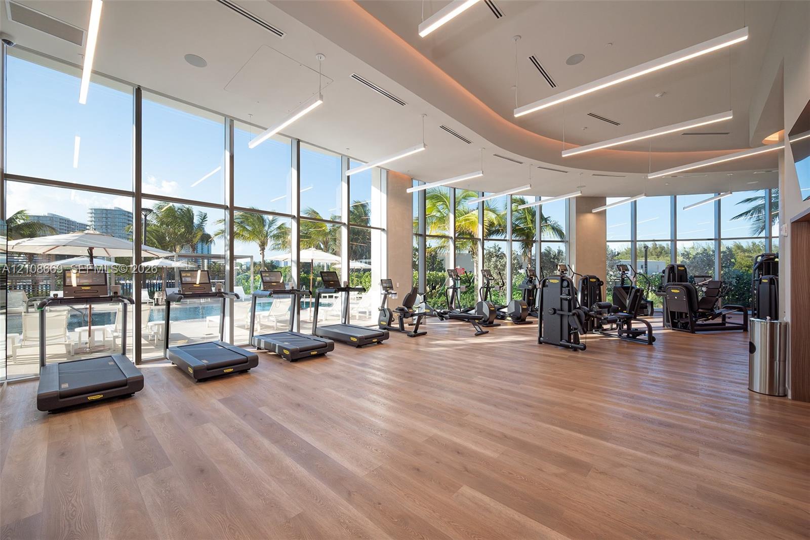 Fitness center featuring floor-to-ceiling glass walls, wood-finish flooring, recessed cove lighting, and linear pendant fixtures