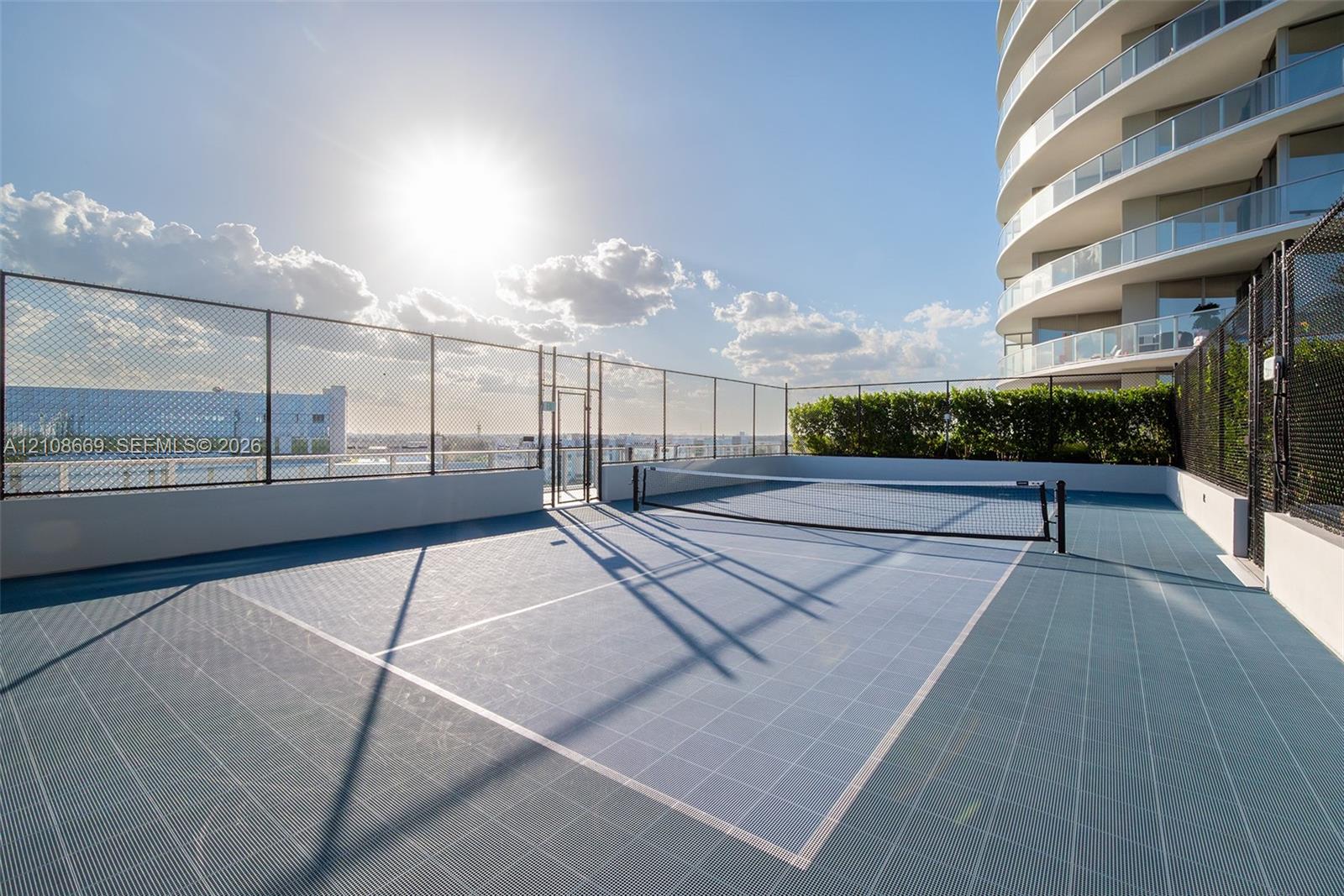 Rooftop sport court featuring blue modular surface tiles, perimeter chain-link fencing, and white masonry walls