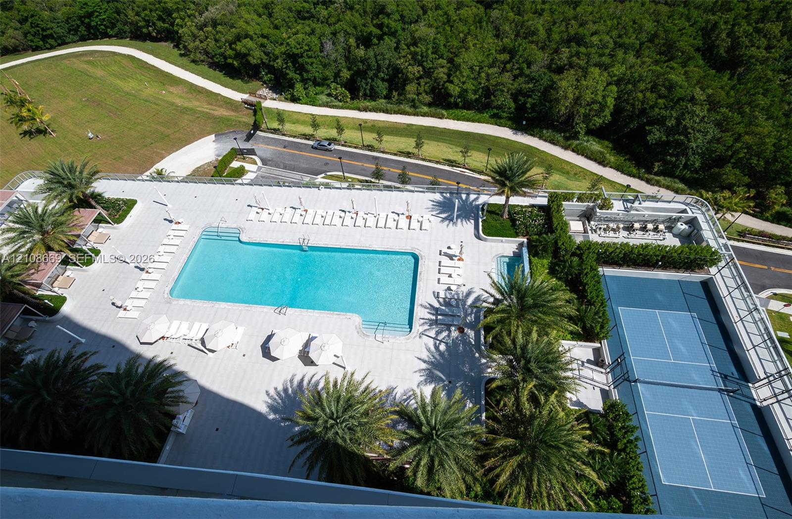 Expansive outdoor recreation deck featuring a swimming pool, separate spa, tennis court, tiled patio surface, and mature palm trees