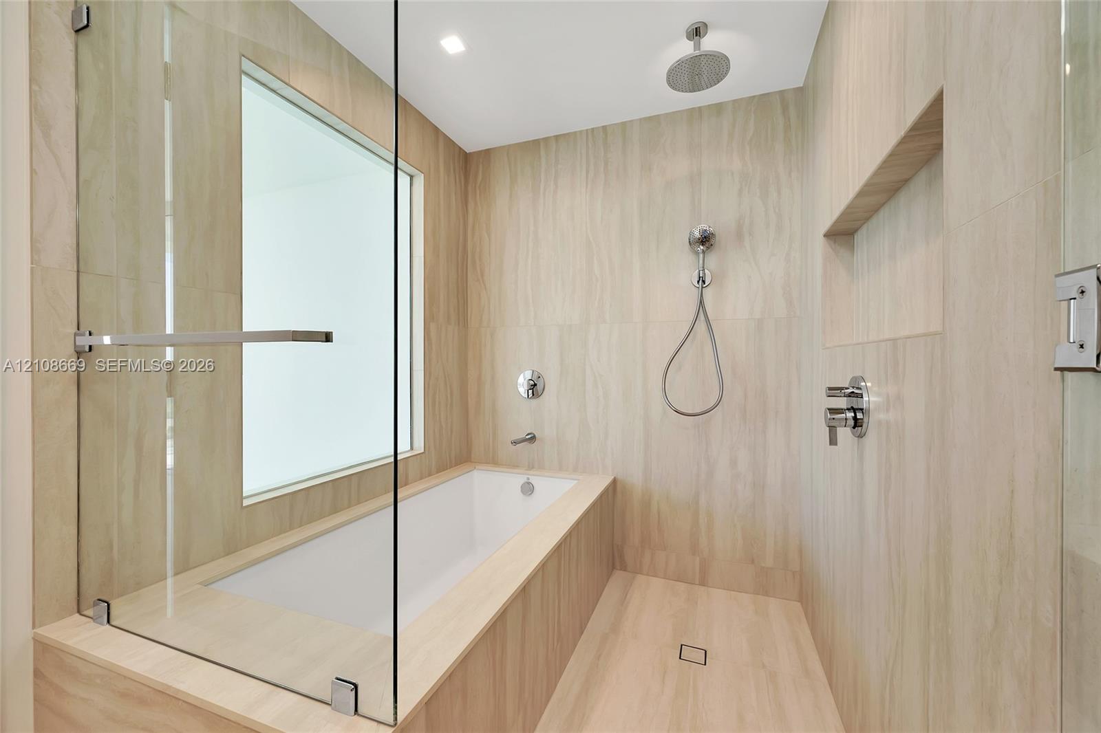 Wet room featuring a built-in soaking tub, large-format tile surround, frameless glass enclosure, ceiling-mounted rainfall showerhead, and recessed wall niche