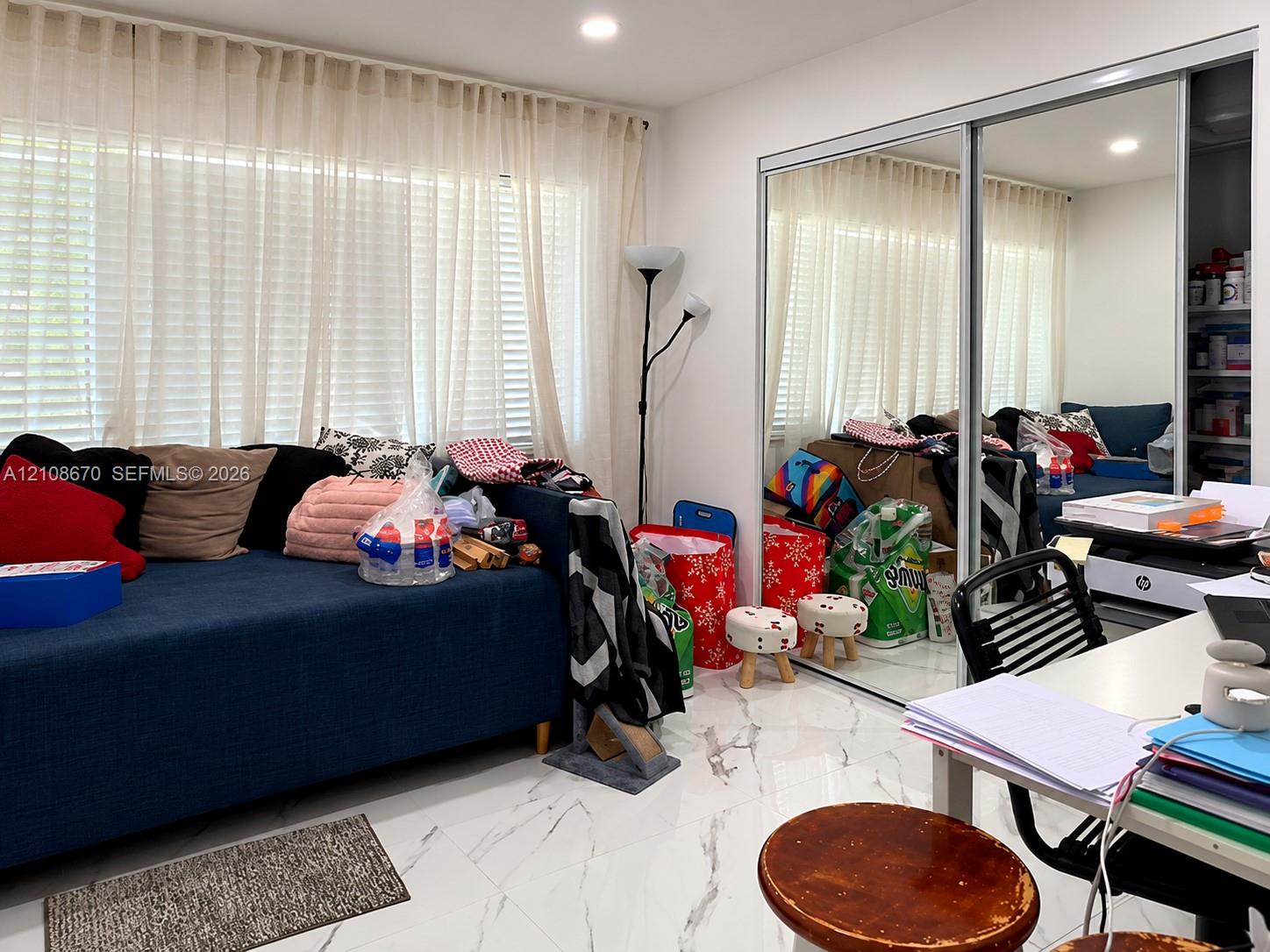 Large-format polished tile flooring with marble-style veining, floor-to-ceiling windows featuring fitted horizontal blinds, and a built-in sliding glass-panel closet door