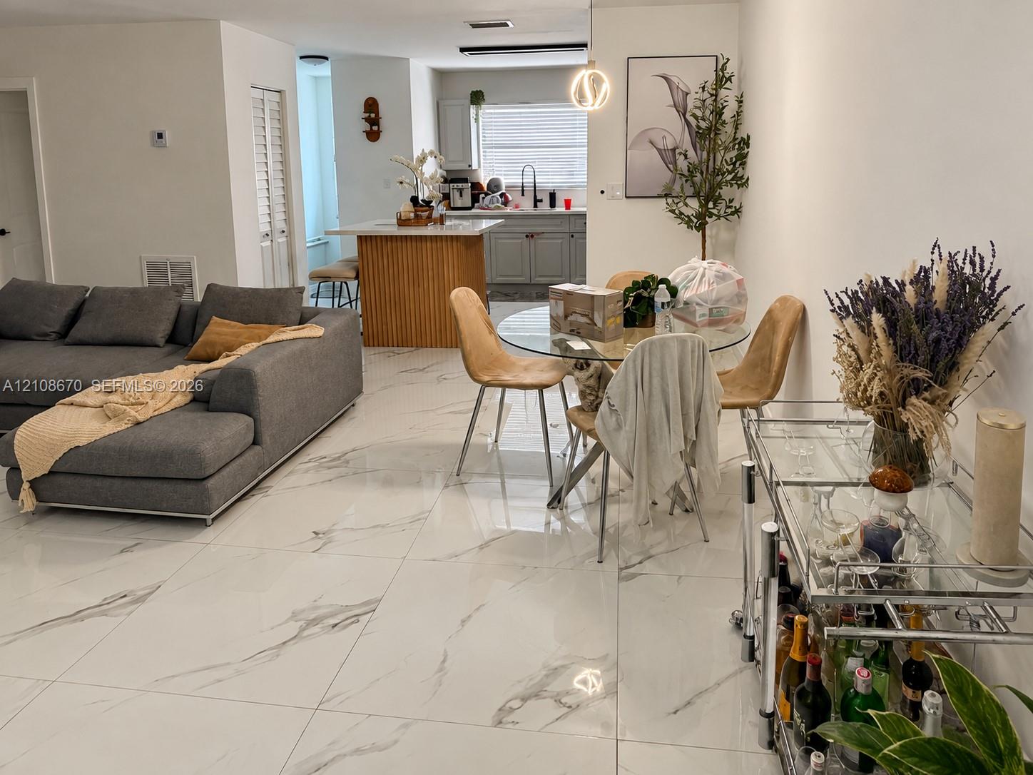 Large-format rectified tile flooring with a marble-finish aesthetic, open-concept kitchen featuring a center island with wood-slat detailing, grey shaker-style cabinetry, and modern spherical pendant lighting