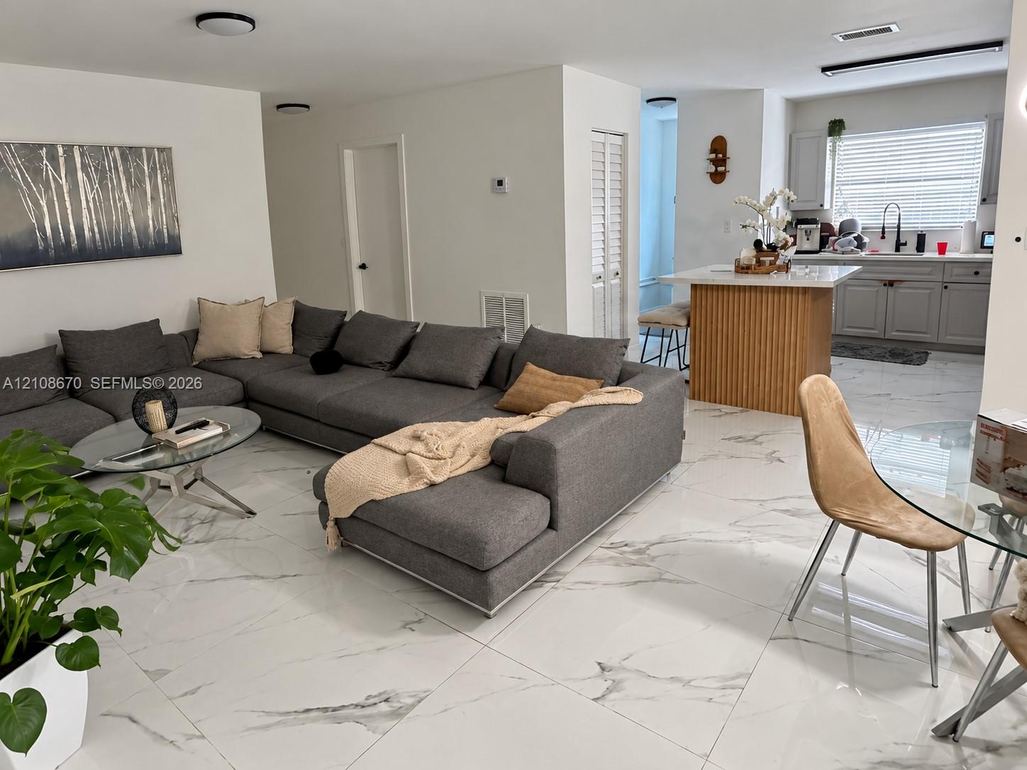 Open-concept interior featuring large-format tile flooring, a kitchen island with fluted wood-finish cabinetry, light gray shaker-style kitchen cabinetry, and recessed ceiling lighting