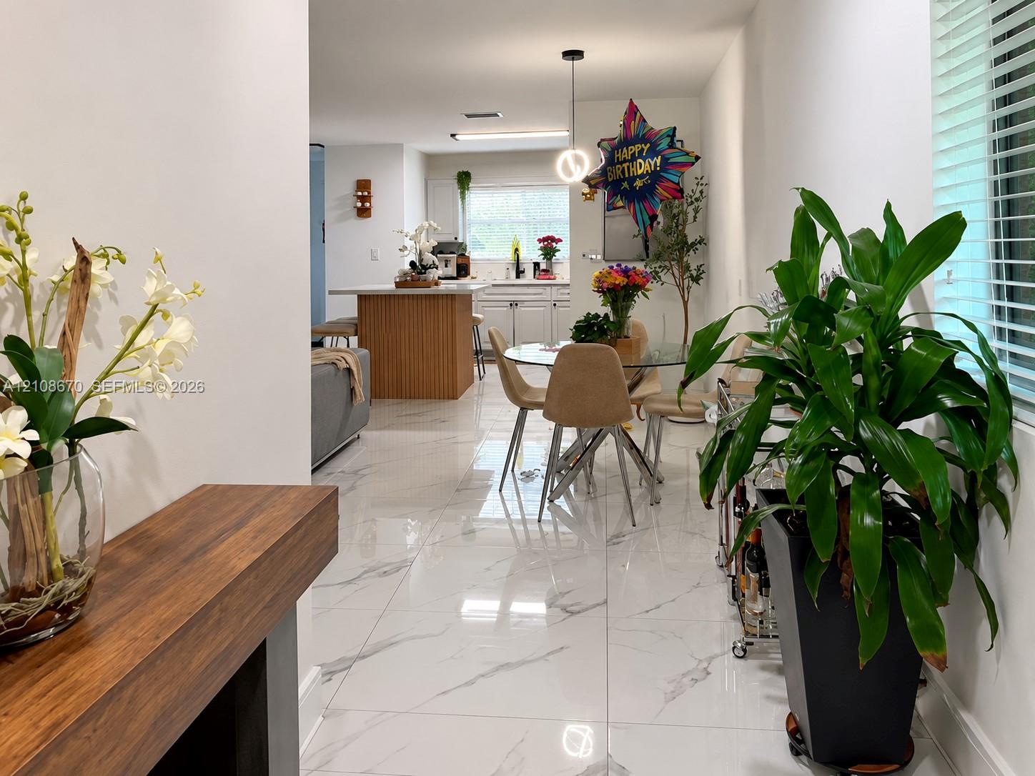 Polished tile flooring with marble-patterned finish, kitchen island featuring vertical wood-slat paneling, and modern spherical pendant lighting