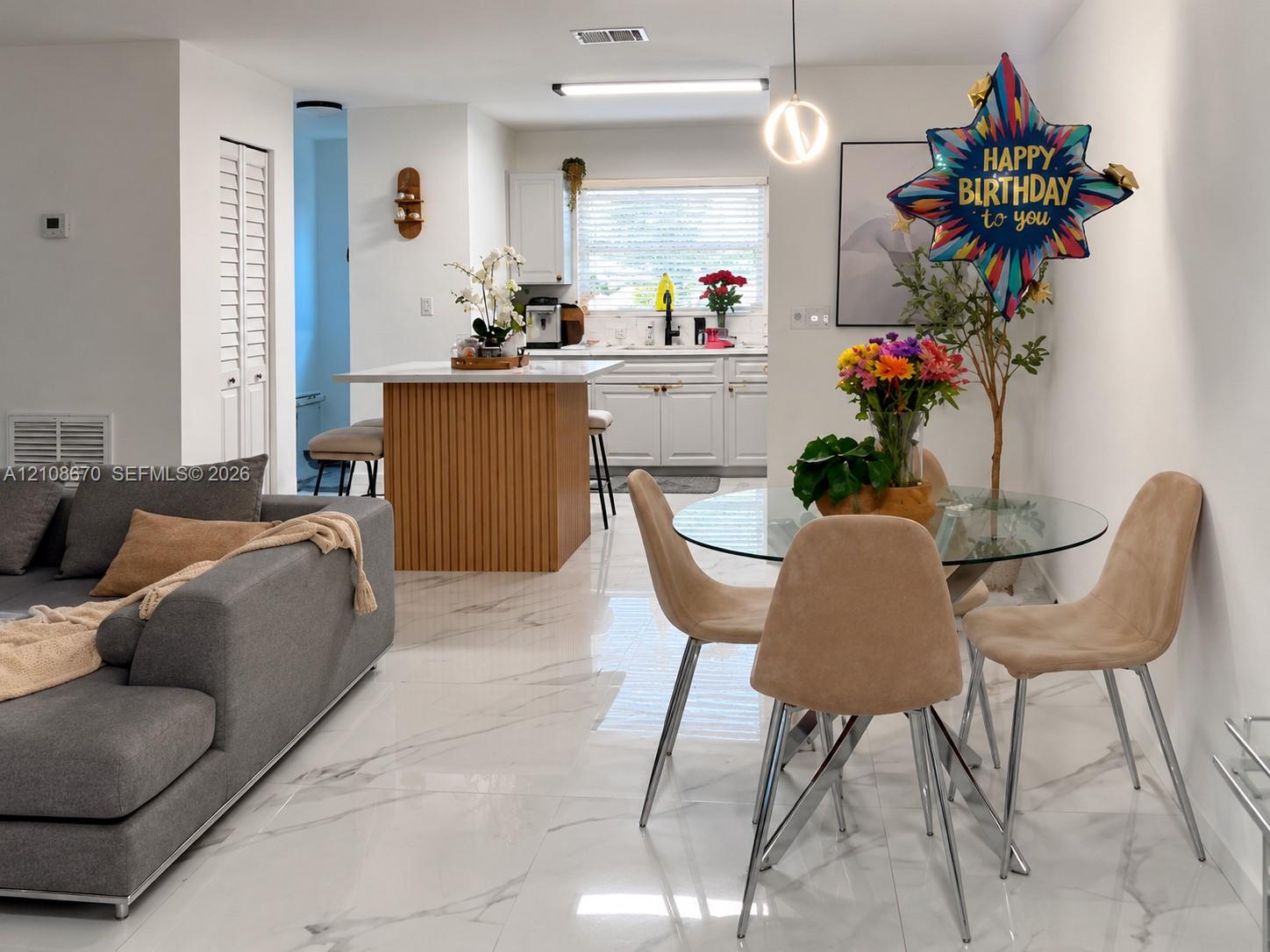 Kitchen featuring white shaker-style cabinetry, a vertical-slat kitchen island with a white countertop, and polished tile flooring Kitchen featuring white shaker-style cabinetry, a vertical-slat kitchen island with a white countertop, and polished tile flooring