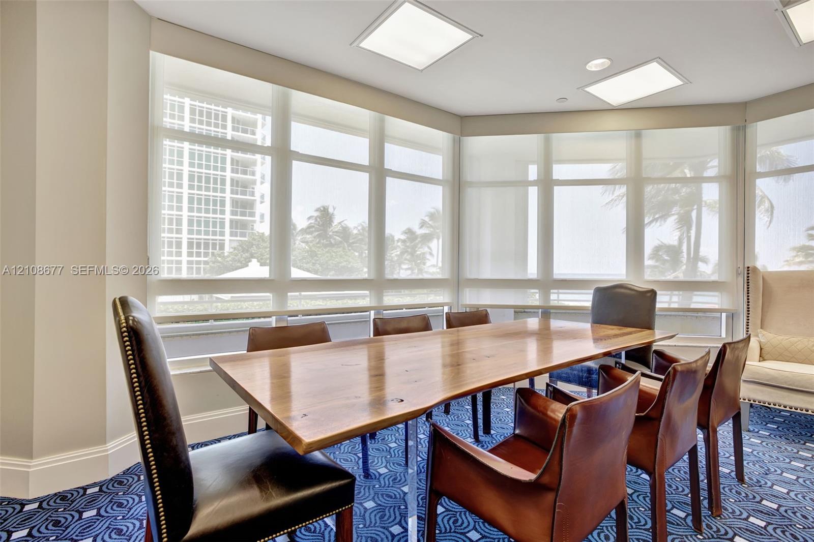 Building community room w/ dining table/ conference room area w/ floor-to-ceiling wrap-around windows featuring light-filtering roller shades and recessed square lighting fixtures