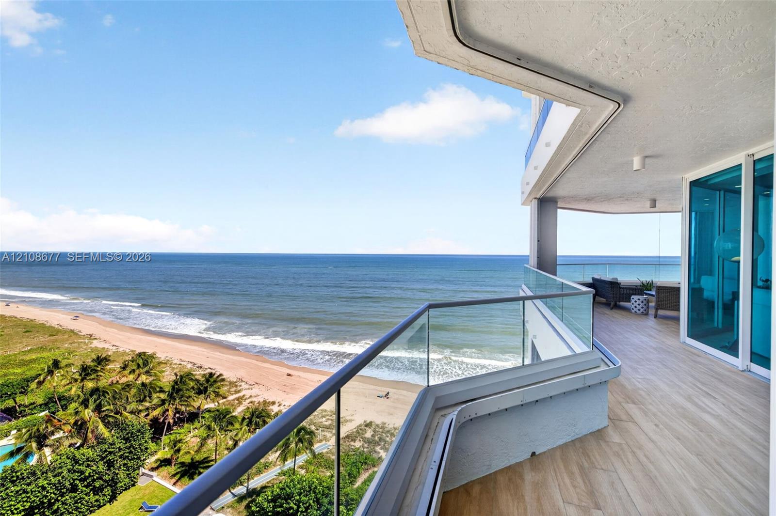 Expansive wraparound balcony featuring glass panel railings, wood look plank porcelain flooring, recessed lighting, and direct oceanfront exposure. Additional protection for your furniture with upgraded accordion shutters.