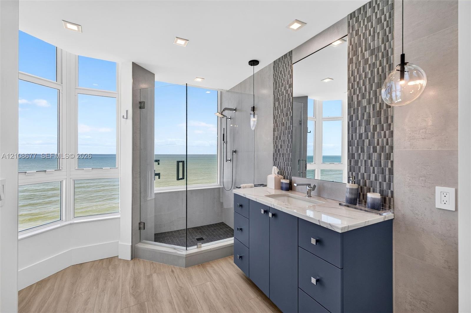 Full Bathroom off guest bedroom / den featuring a wood look plank porcelain floor, navy blue vanity with a stone countertop, glass-enclosed shower with tiled flooring, mosaic tile backsplash, and floor-to-ceiling windows