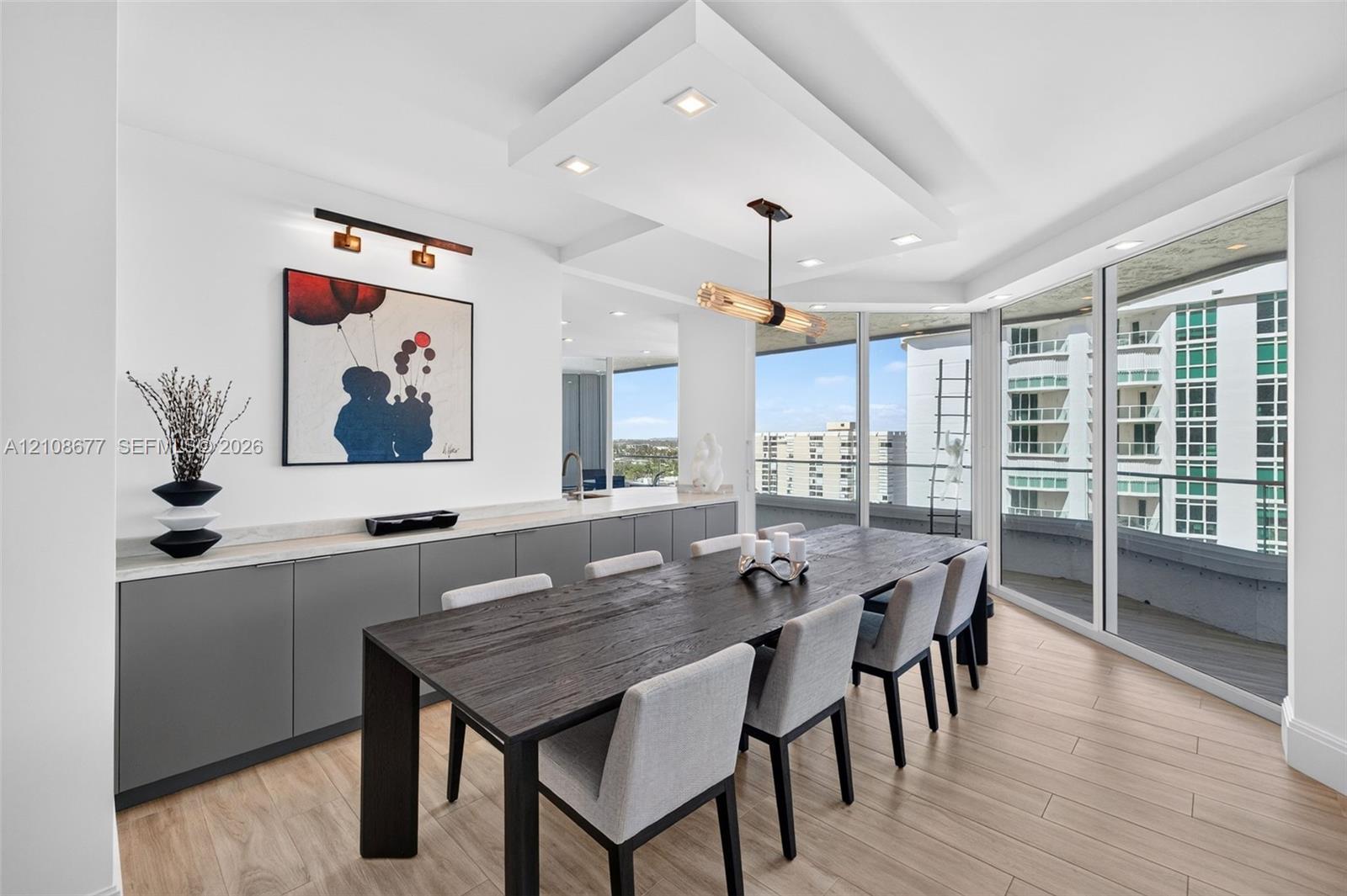 Floor-to-ceiling impact windows, recessed architectural ceiling detail with integrated lighting, wood look plank porcelain flooring, custom cabinets with gorgeous neutral stone surfaces, and a beautiful suspended linear dining fixture. Light filtering remote operated shades with Bandalux