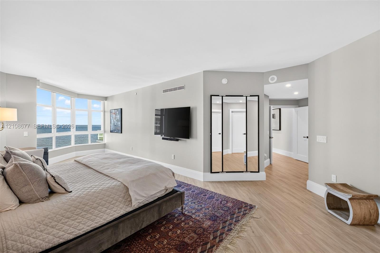 Expansive window wall with water view, wood look plank porcelain flooring, and built-in mirror paneling. Light-filled ovesized primary bedroom featuring floor-to-ceiling impact windows, wood look plank porcelain flooring, and wall-mounted light sconces. Extra sitting area, office space, gym or nursery. This is said to be the only unit in the building with a built in primary sitting area (instead of small balcony space). Original developer enclosed the space for first owner. Double layered remote shades