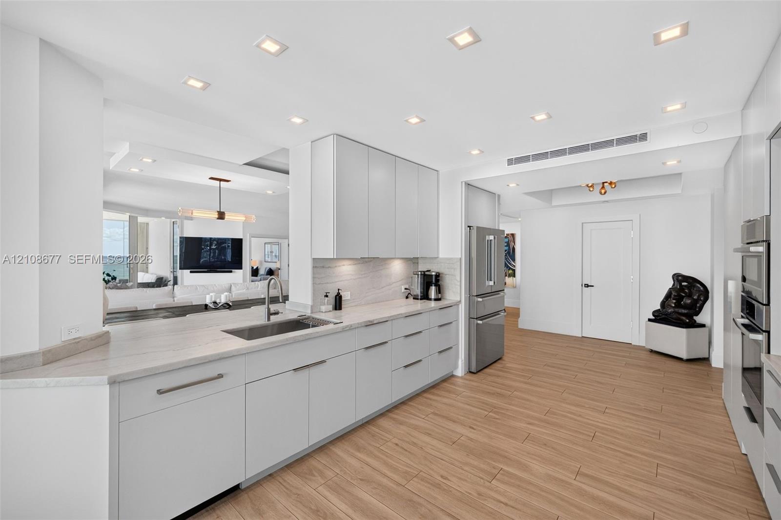 Kitchen featuring flat-panel cabinets, light-toned stone counters, stainless appliances including a wall ovens, recessed lighting, and wood look plank porcelain flooring - pass through to dining area and buffett / serving area Kitchen featuring flat-panel cabinets, light-toned stone counters, stainless appliances including a wall ovens, recessed lighting, and wood look plank porcelain flooring - pass through to dining area and buffett / serving area